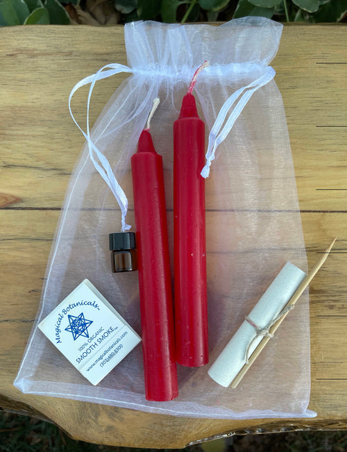 Two red candles in a clear drawstring bag with a match and a card on a wooden surface.